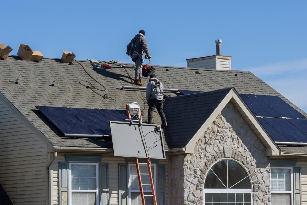 Solar Technician workers installing alternative energy photovoltaic solar panels on house roof